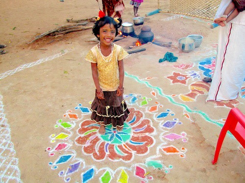 A proud girl stands over her kolam